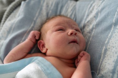 Yeni doğmuş bir bebek, sıcak, açık mavi bir battaniyeye sarılmış bir yatakta dinleniyor. Bebek tuhaf bir ifadeyle yukarı bakıyor, eski hayatın harikasını ve masumiyetini somutlaştırıyor..