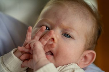 A curious baby gazes at her hands with a joyful expression, showcasing her light brown hair and blue eyes. clipart