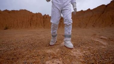 Beyaz takım elbiseli ve kasklı bir astronot kraterin rahatlığı boyunca hareket ediyor. Slow Motion astronotu Mars 'ta kameraya doğru yürüyor..