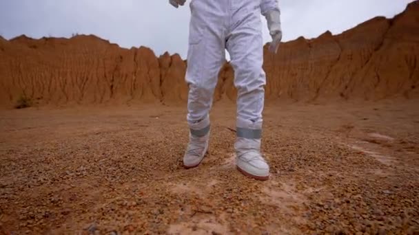 一名身穿白色西装 头戴头盔的宇航员沿着火山口的凸起处移动 缓慢运动的宇航员走向火星上的相机 — 图库视频影像