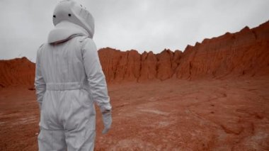 Uzay giysisindeki astronot gezegen kraterine bakıyor. Uzak kırmızı yüzey gezegenindeki uzay giysisi giymiş bir adamın omuz ve dikiz açıcı görüntüsü..