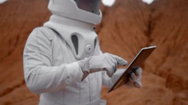 Astronot Mars yüzeyinde dijital bloknotlarla çalışıyor. Kraterin içindeki uzak gezegenlerin çevresine bakıyorum. Tablet bilgisayarındaki kostüm ve miğfer koruma veri analizi.