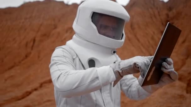 宇航员正试图修理一个不工作的石碑 在遥远的火星上 一位身穿白衣 头戴头盔的宇航员试图用平板电脑探测火星表面 — 图库视频影像