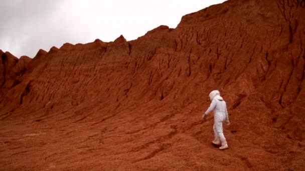 火星表面追跡無人機ショットを探索している宇宙飛行士 認識できない男で白い宇宙服とヘルメット歩行に赤い惑星のクレーター — ストック動画