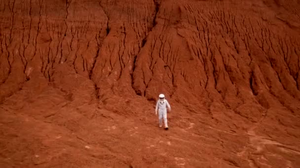 遠くの惑星の赤い表面を歩く宇宙飛行士のドローンのショット 酸性雨のない未知の宇宙の場所と宇宙の風景 — ストック動画