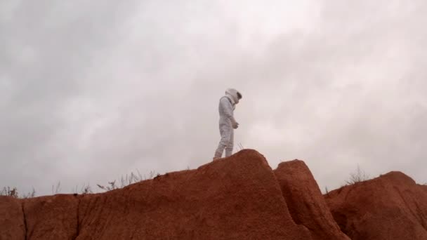 宇宙飛行士は 遠くの惑星の表面の上の丘に立って見て回る 砂の土壌 酸性の雰囲気と植民地化のための地球上の雨 — ストック動画