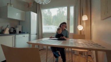 Şefkatli bir anne, küçük oğluna mutfak masasında oturan parlak resimler gösterir. Kadın ve küçük çocuk hafta sonunu büyük yazlık evde geçirirler.