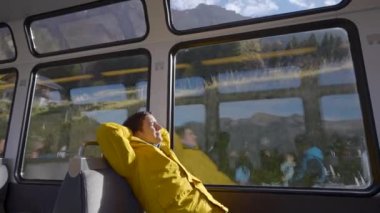 Erkek turist büyük pencerenin yanındaki koltuğa yaslanır ve trenle gezinin tadını çıkarır. Erkek yolcu, İsviçre dağlarını demiryolu taşımacılığıyla geçiyor.
