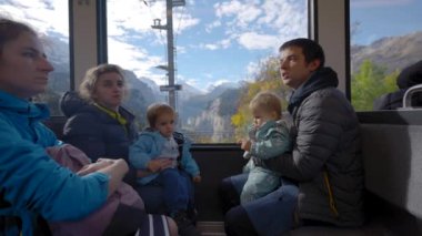Küçük çocuklu büyük bir aile güneşli bir günde dağlık arazide trenle seyahat eder. Çocuklu aileler İsviçre 'nin manzaralı dağlarına bakıyorlar.
