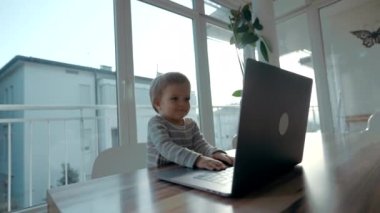 Happy Toddler gülümseyen dizüstü bilgisayarın tuşlarına basmaya çalışıyor. Masum küçük çocuk panoramik balkon karşısında aletleri incelemekten zevk alıyor.