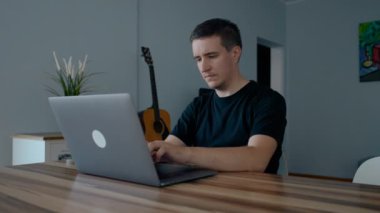 Odaklanmış erkek programcı evde dizüstü bilgisayarda yeni web sitesi geliştirir. Genç adam şık bir odada ahşap masada oturuyor ve yavaş çekimde çalışıyor.