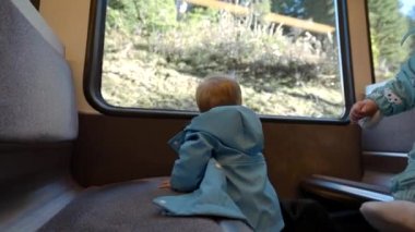 Kız kardeşi annesinin kucağında otururken, küçük çocuk oturmuş vagonun camından dışarı bakıyor. Büyük aile sonbahar gezisinin ve İsviçre 'nin doğasının tadını çıkarıyor.