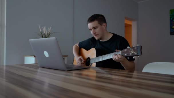 男人在笔记本电脑上玩吉他看教育视频 初学者音乐家学会使用乐器 坐在木桌旁边慢动作 — 图库视频影像