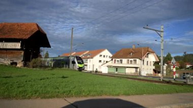 Modern yolcu treni İsviçre 'nin küçük bir kasabasından geçiyor. Güneşli bir günde bulutlu gökyüzünün altında altyapı ve manzaralı kırsal alan