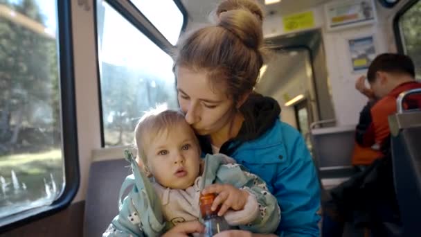 慈爱的母亲吻着坐在窗边明亮的背光下的小女儿 女人和女婴喜欢乘火车特写慢镜头旅行 — 图库视频影像