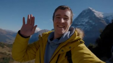 Aile ve arkadaşlarla İsviçre seyahati hakkında telefon görüşmeleri videosu kaydeden bir adam. Turist dalgaları. Kameraya yakın çekim konuşuyor.