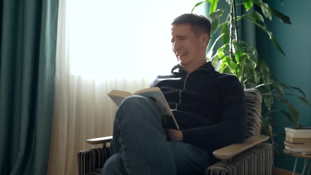 Smutny Mężczyzna Luźnych Ubraniach Siedzi Kanapie Czyta Książkę Podczas Odpoczynku — Wideo stockowe
