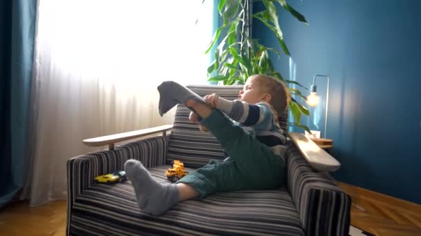 托德勒坐在舒适客厅里的扶手椅上 想穿上袜子 慢镜头拍摄的广角娃娃为我们提供了这个愉快时刻的迷人景象 — 图库视频影像