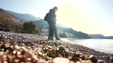 Denizin çakıl taşlı kıyılarında yürüyen bir anne ve oğulun odaksız silueti. Yavaş çekim, güneşli sahneye rüya gibi bir kalite katar..