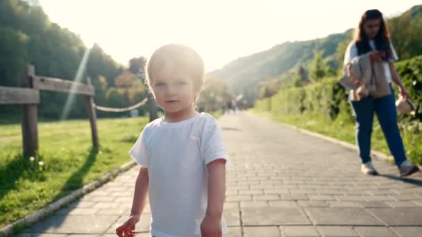 小さな男の子が女性の隣の歩道を歩いていて 仲間と動きの典型的な場面を示しています — ストック動画