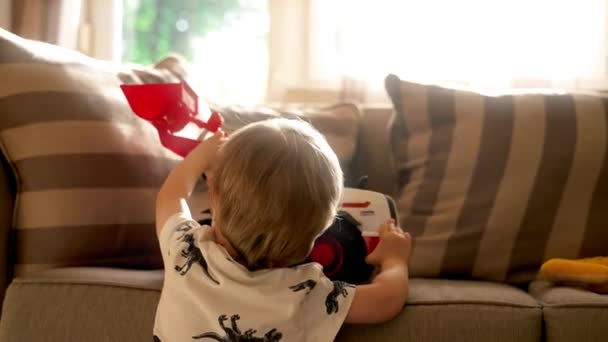 ソファに座っている若い男の子をキャプチャするビデオ 活気に満ちたおもちゃのペアを握る — ストック動画