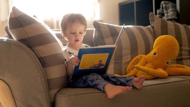 Маленький Хлопчик Сидить Дивані Повністю Поглинутий Читанням Книги — стокове відео