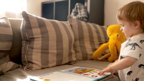 在这个视频中 可以看到一个小男孩一边看书 一边在客厅舒适的沙发上做运动 一边自学 — 图库视频影像