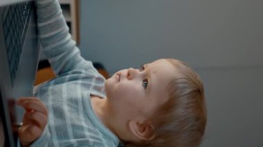 Odaklanmış küçük çocuk masadaki modern dizüstü bilgisayarda çizgi film izliyor. Sarışın çocuk hafta sonu sabahını evde aletle dikey çekim yaparak geçiriyor..