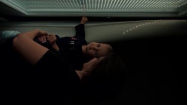 Anne kollarındaki sevimli çocuk yatak odasını aydınlatmak için pencerenin perdelerini açmayı öğreniyor. Kadın ve küçük çocuk güneşli bir sabahın keyfini çıkarın. Yakın çekim dikey çekim..