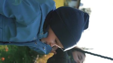 Sevimli küçük çocuk otelin bahçesinde annesini sallıyor. Şapkalı çocuk, güneşli bir günde annesini kırsalda ağırdan alıp eğlendiriyor..