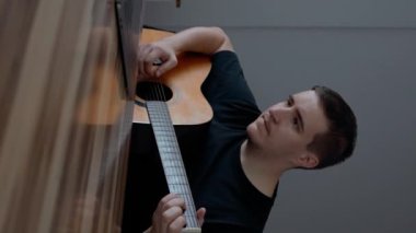 Adam dizüstü bilgisayarda eğitim videoları izlerken gitar çalıyor. Acemi müzisyen ahşap masada ağır çekimde oturup müzik aleti kullanmayı öğreniyor..