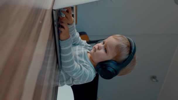 Serious Toddler Headphones Imitate Working Modern Laptop Sitting Wooden Table — Stock Video
