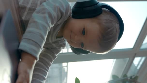 Очаровательный Малыш Наушниках Типа Клавиатуре Ноутбука Сидит Напротив Балкона Любопытный Стоковое Видео
