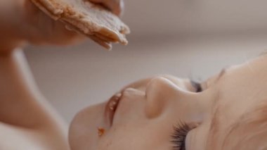 Yemek sırasında hareketlerini ve ifadelerini sergileyen, bir parça yemek yiyen küçük bir çocuğun videosu. Dikey görüntüler.