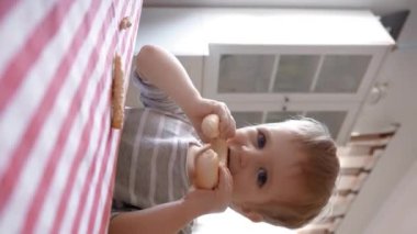 Küçük bir çocuğun gastronomi dünyasına dalışını izleyin, bir masaya oturup çeşitli lezzetli yiyeceklerle şımarmasını. Dikey görüntüler.