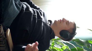 Kanepede oturan ve evde rahat bir odada dinlenirken kulaklıkla müzik dinleyen gündelik elbiseli genç bir erkek görüntüsü..