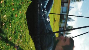 Şirin çocuk, babamı otelin bahçesindeki sallanan yuvada sallamaya çalışıyor. Adam sonbahar tatilinde oğluyla kırsal kesimde eğleniyor. Yavaş çekim dikey çekim..