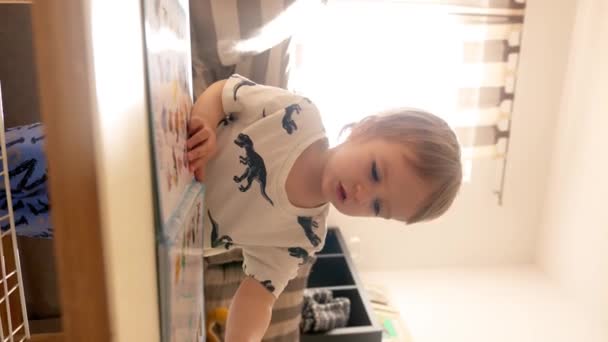 一个小男孩坐在一个舒适的客厅里的桌子旁 一边教书本 一边用钢笔做练习 垂直镜头 — 图库视频影像