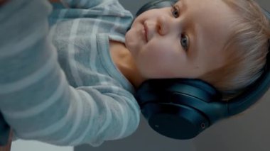 Aktif çocuk, kulaklıkla dizüstü bilgisayarda yazarken müzik dinliyor. Odaklanmış küçük çocuk masada oturur oturma odasında yeni yetenekler öğrenir dikey çekimler.