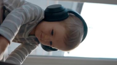 Kulaklıklı heyecanlı küçük çocuk dizüstü bilgisayarın klavyesinde yazarken güler. Şirin çocuk, modern teknolojiyi seviyor. Masada yavaş çekimde, dikey görüntülerde oturuyor..