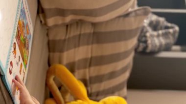 Bu videoda, küçük bir çocuk kitap okurken ve oturma odasındaki rahat bir kanepede egzersiz yaparken görülebilir. Dikey görüntüler.