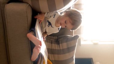 Küçük bir çocuk bir kanepede oturur, kitap okumaya dalmıştır. Dikey görüntüler.