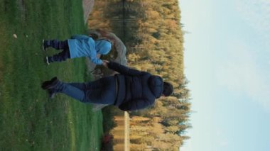 Kadın ve çocuk, sonbahar ormanı yakınlarındaki göle doğru yeşil çayırlarda yürürken el ele tutuşuyorlar. Anne ve oğlu kırsal alanda hafta sonunun tadını çıkarıyorlar. Yavaş çekim, dikey çekim..