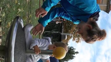 İsviçre, Bern - 15 Ekim 2022: Anne, küçük kızının sonbahar günü girdapta dönüşünü izliyor. Aileler, kalabalık halk parkında aktif çocukları eğlendiriyorlar..