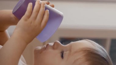 Küçük bir çocuğu mor bir bardaktan içerken gösteren bir video. Dikey görüntüler.