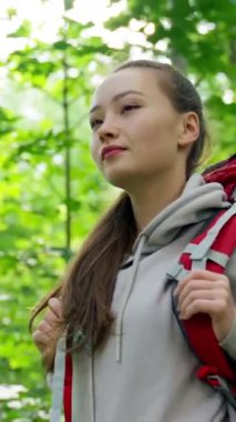 Kırmızı sırt çantası takan genç bir kadın yoğun bir ormanda gülümseyerek yürüyüşe çıkıyor. Kahverengi saçlı bayan sabah ağır çekimde vahşi doğayla birleşmeyi seviyor..