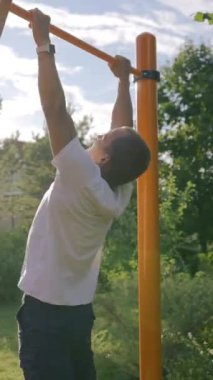 Orta yaşlı sporcu yetişip kendi bahçesinde direğe asılmış. Olgun jimnastikçi sağlıklı yaşam tarzını sever ve arka tarafta dikey çekimde egzersiz yaparken formda kalmaya çalışır..