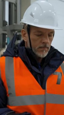 Gri sakallı mühendis depo öngörüsüne bakmak için dizüstü bilgisayar kullanıyor. Beyaz kasklı olgun bir adam depo terminalinde dikey yavaş çekimde dikey çekim yapıyor..