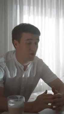 Genç adam kız arkadaşıyla video görüşmesinde dizüstü bilgisayarla parlak pencerenin karşısında oturuyor. Adam evde dijital iletişimden hoşlanıyor. Yakın çekim dikey çekim..