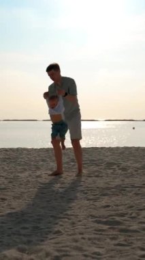 Suyun babası çocuğu okyanus kıyısındaki kulplardan çevrelemiş. Bir ebeveyn ve çocuk için mutlu bir tatil kavramı, çocuklarla dikey çekim yapılan bir zaman..